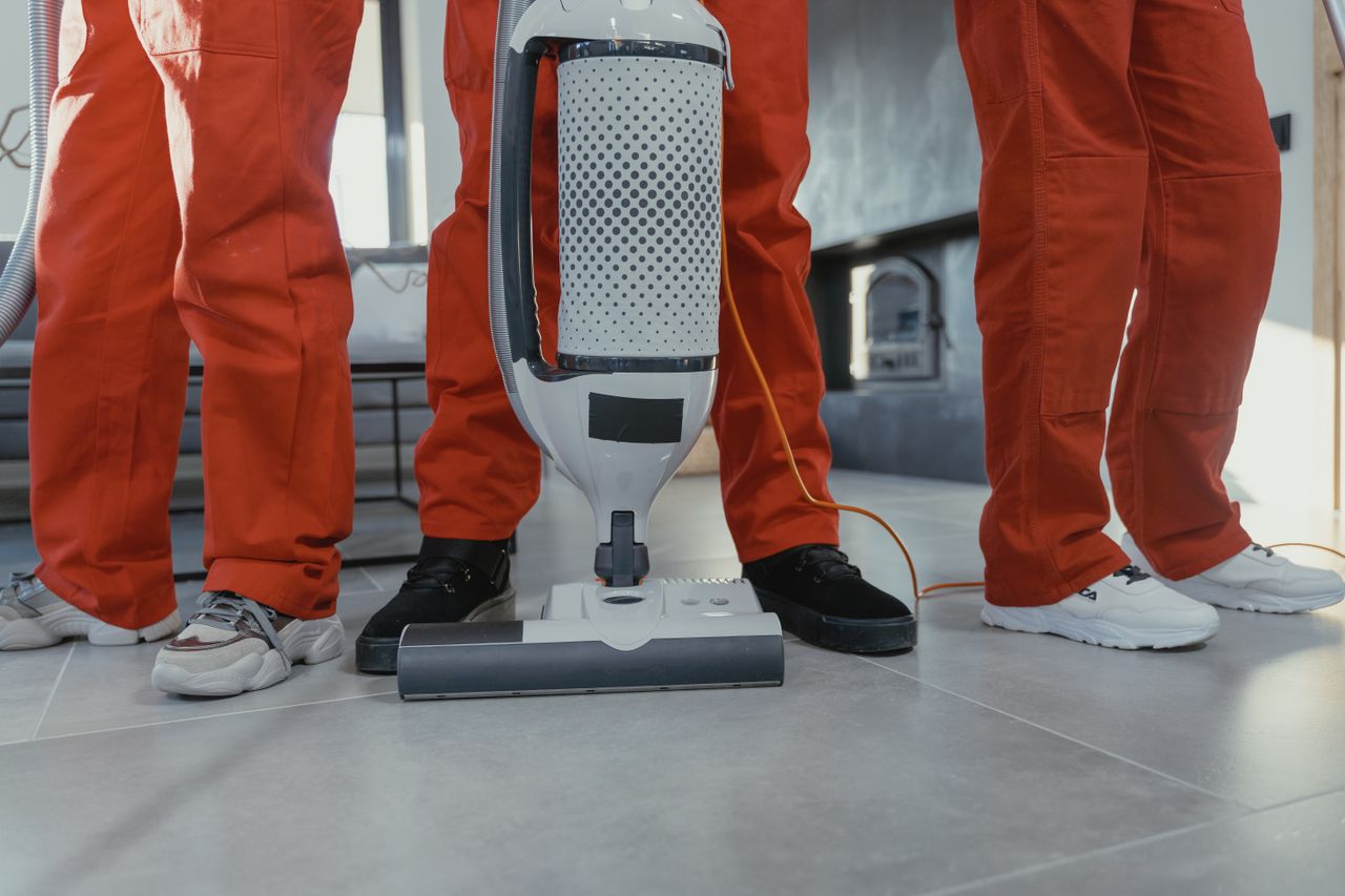 about-us Team of professional cleaners in red uniforms using a vacuum cleaner indoors.