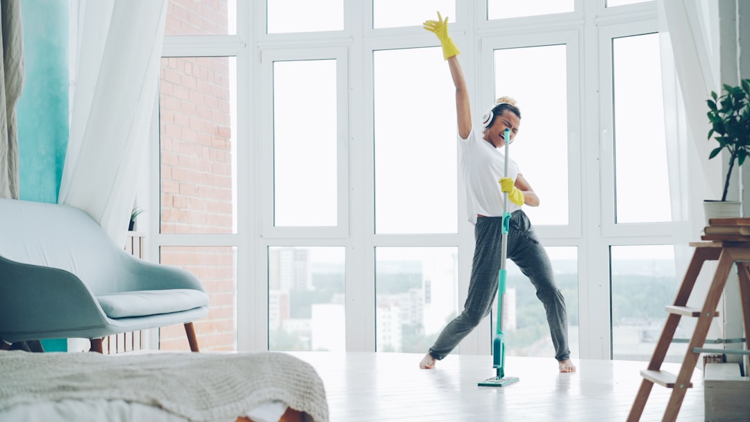 services-03 Joyful young woman is enjoying music in headphones, dancing and singing during routine cleanup at home, girl is mopping floor and having fun. People, technology and houses concept.