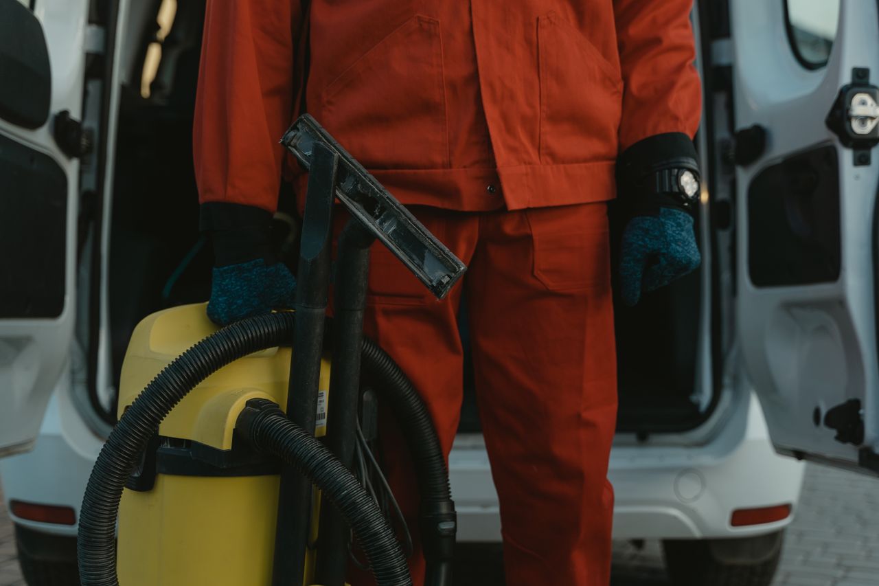 heros-img A professional cleaner in a red uniform holding a vacuum near a van, ready for service.